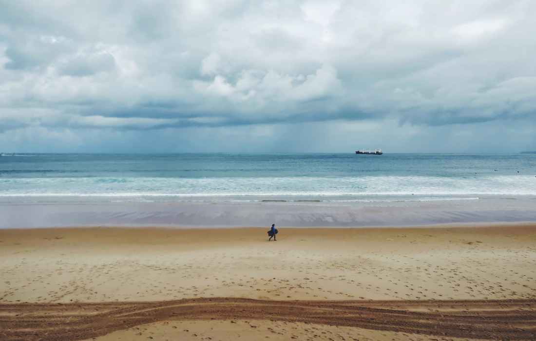 person walking on sand near body of water