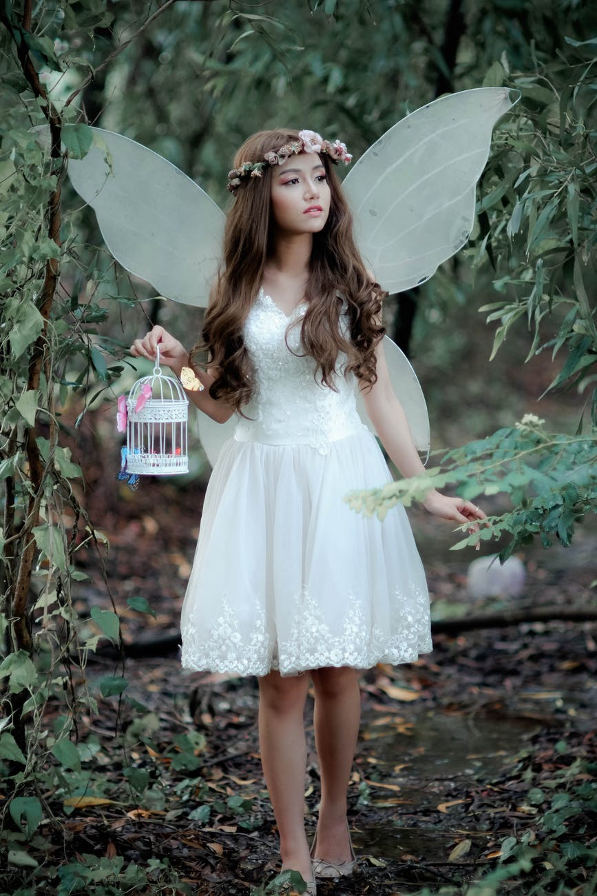 girl holding white birdcage standing behind trees
